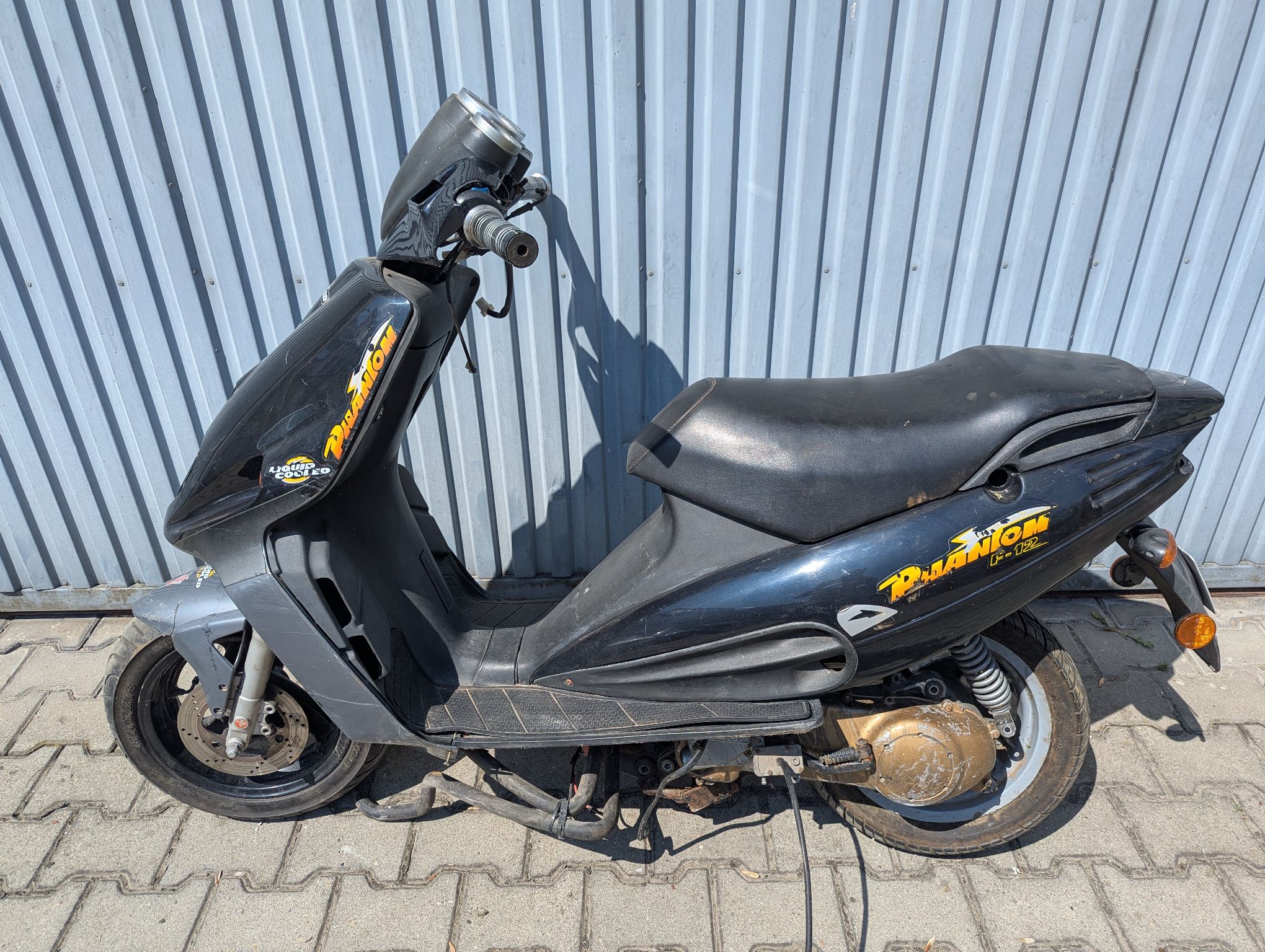 Lewa strona czarnego motoroweru Malaguti. Zwisające gumowe przewody, odkręcony tylny amortyzator