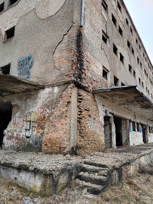 Popękane ściany, widać cegły, graffiti, zniszczone wejście, schody.
