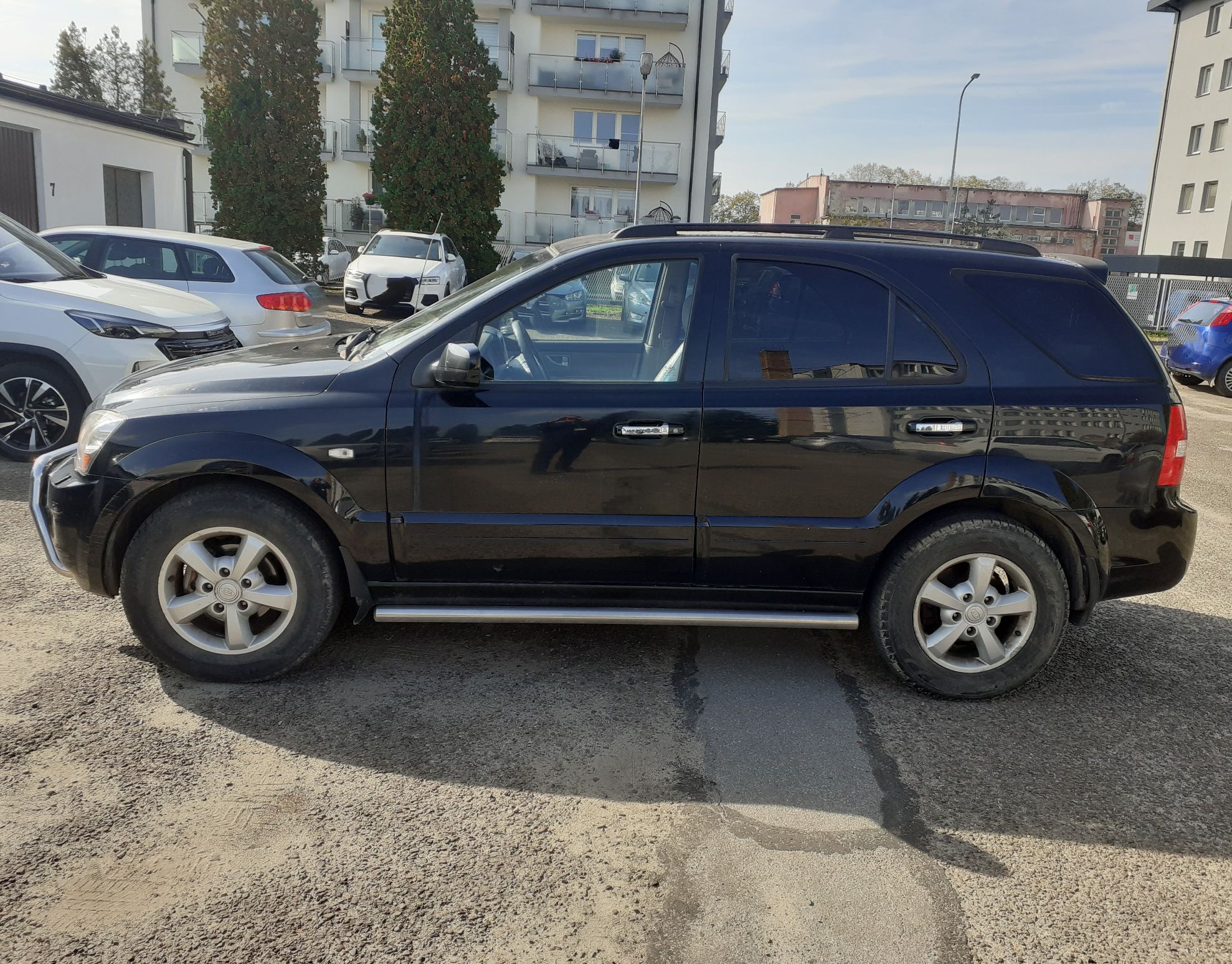 Czarny SUV Kia Sorento widok od strony kierowcy. Widoczne srebrne progi boczne i pięcioramienne felgi aluminiowe.