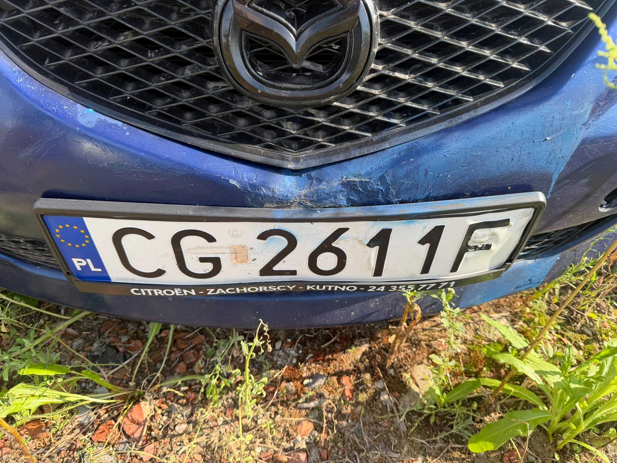 Przedni niebieski zderzak pojazdu z widocznym uszkodzeniem.