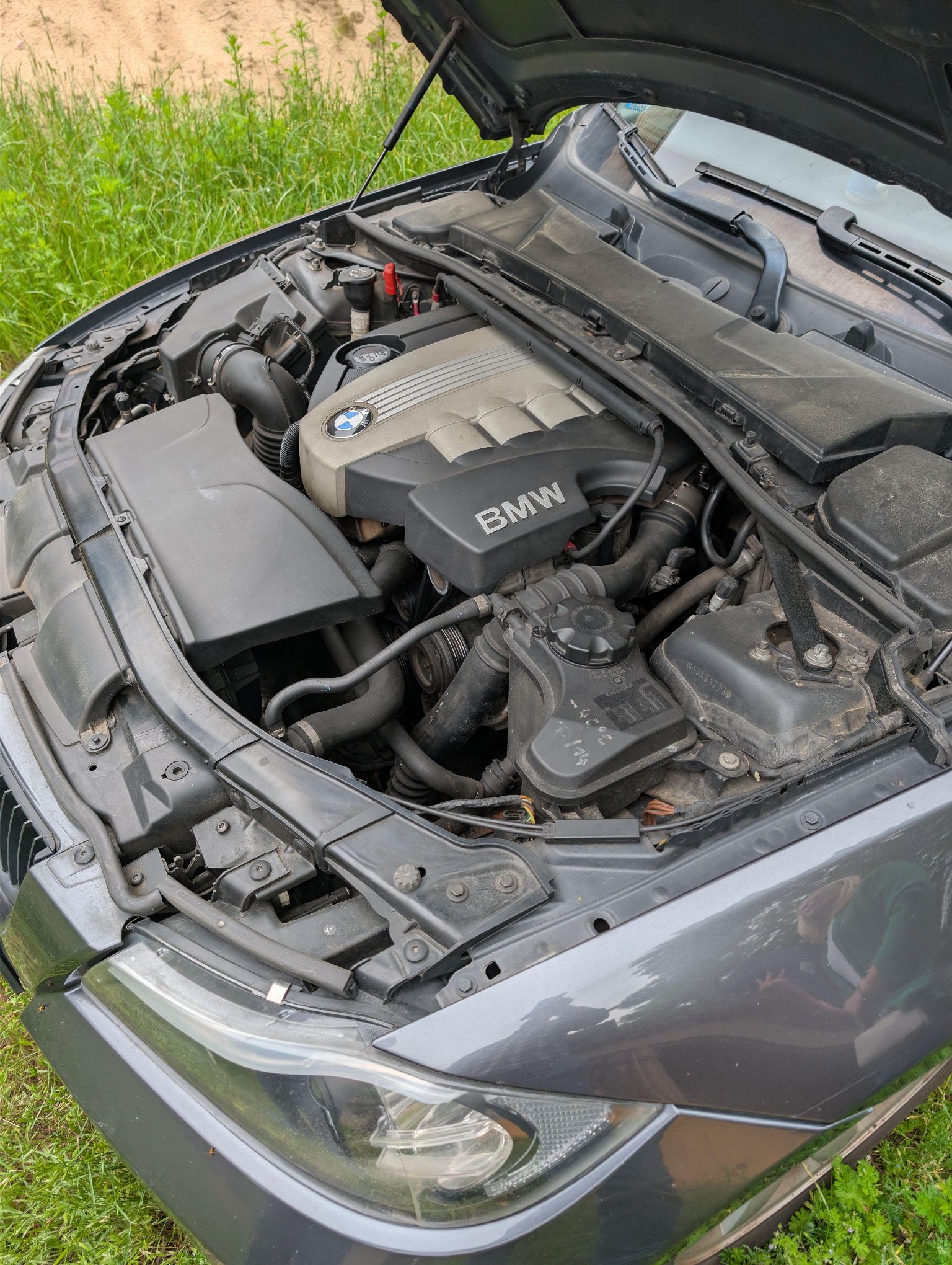 Otwarta komora silnika samochodu BMW. Widoczny jest silnik z osłoną z logo BMW.