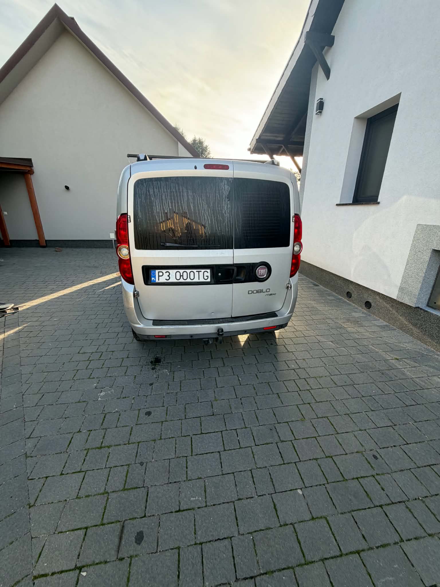 Fiat Doblo z 2010 roku o charakterystycznej bryle. Auto ma dużą przednią szybę, pionowe reflektory i przesuwne drzwi boczne.