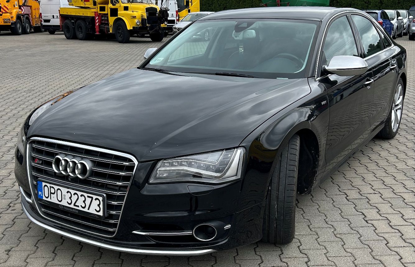 Przód i lewa strona pojazdu. Na przodzie jest duży, chromowany grill z czterema pierścieniami marki Audi oraz oznaczeniem S8.