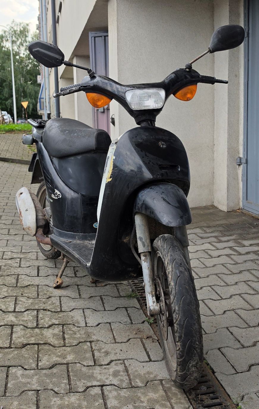 Motorower koloru czarnego. Widok z przodu. Dwa lusterka wsteczne na kierownicy. Prawe lusterko uszkodzone.