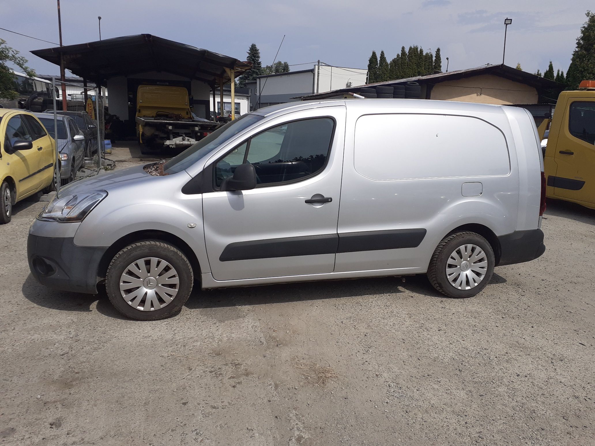 Srebrny Citroën Berlingo, ujęcie z boku od strony kierowcy. Widoczne czarne listwy ochronne i kołpaki.