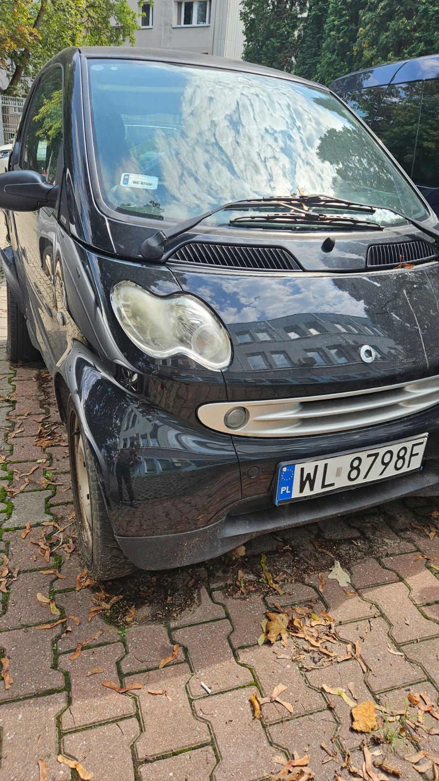 Na zdjęciu czarny samochód Smart, Widok z przodu z lewej strony. Widoczne jest przednia szyba, reflektory, przedni zderzak.
