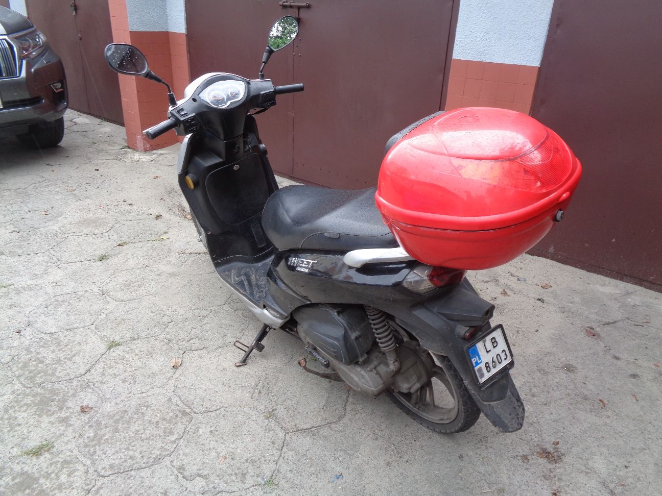Widok na motorower (lewy tył), czerwony kufer.