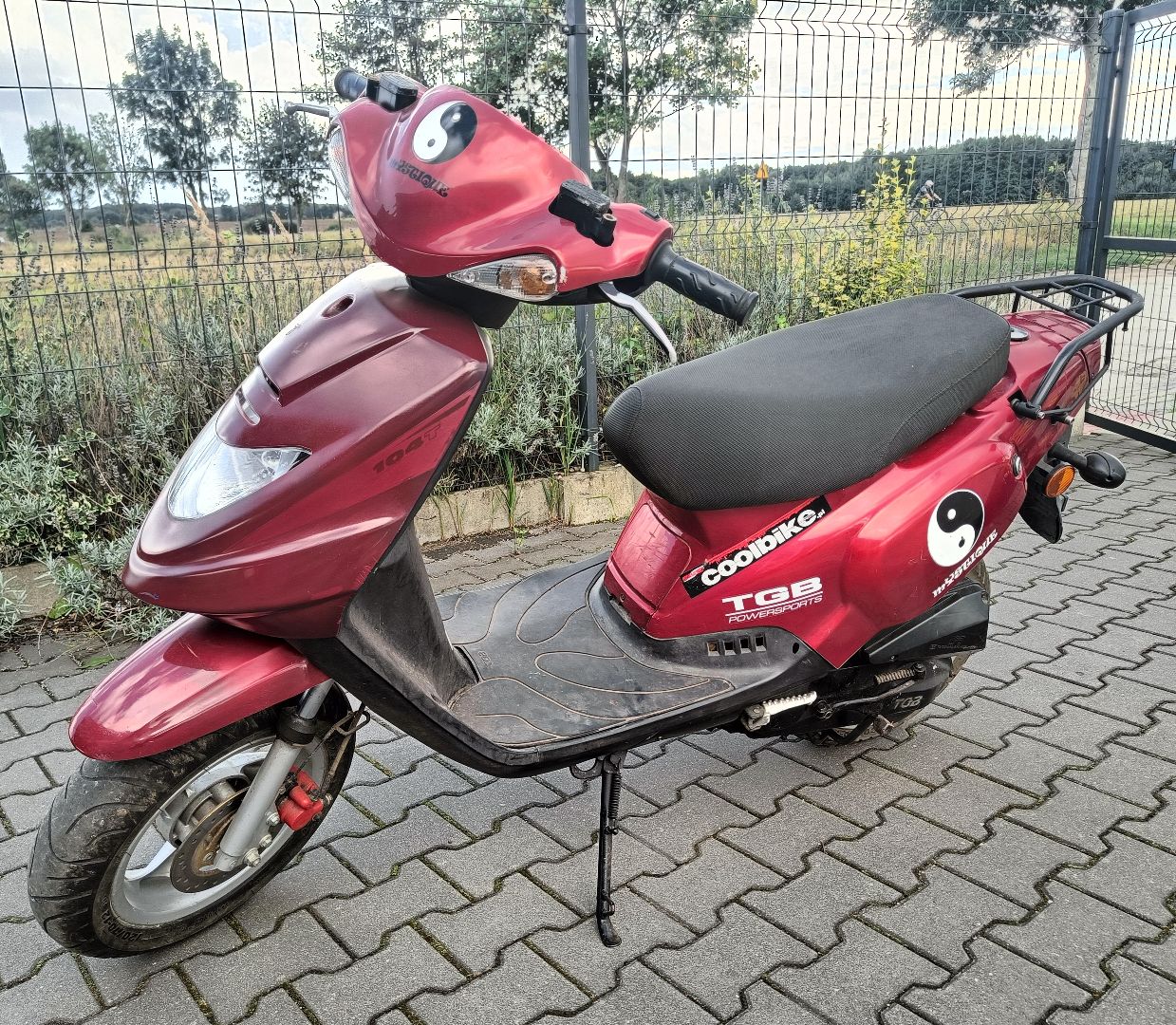Przód oraz lewy bok motoroweru w kolorze czerwonym, widoczne zadrapania na obudowach pojazdu.
