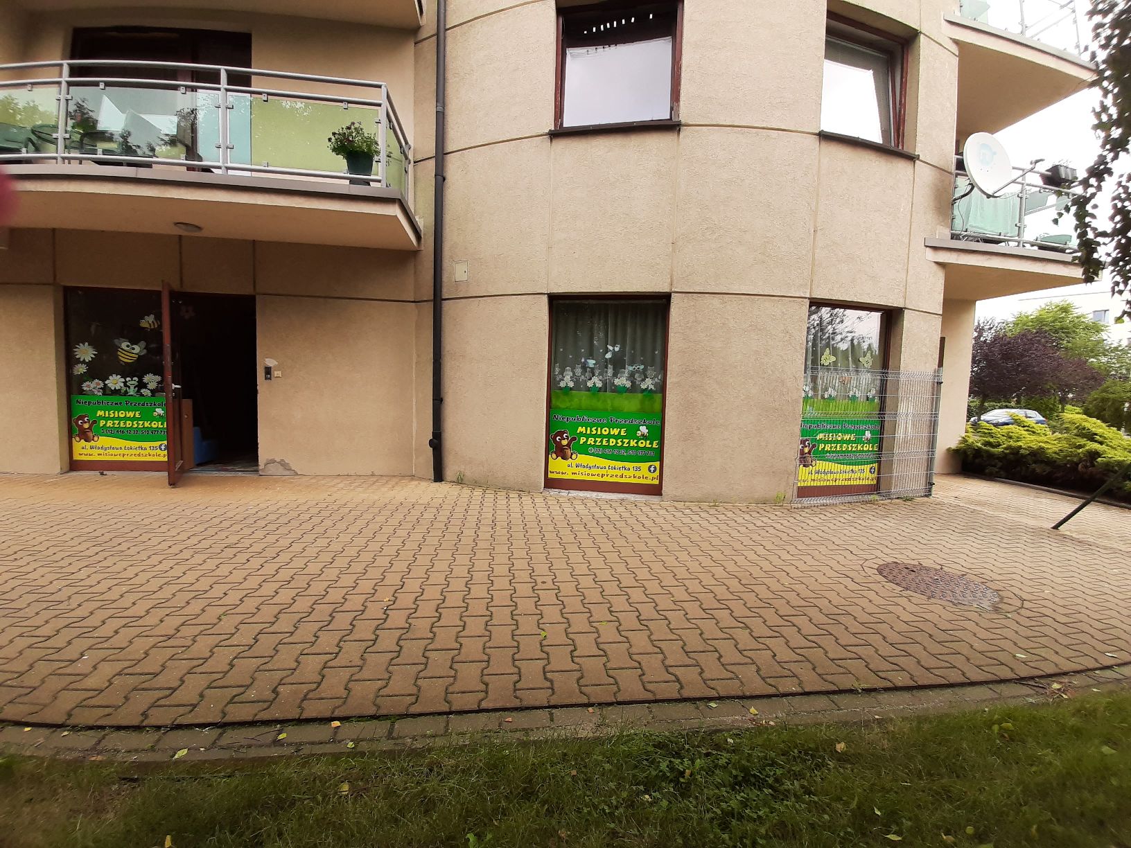 Lokal usługowy na parterze 4 kondygnacyjnego budynku. Widok na drzwi wejściowe oraz dwa okna witrynowe.