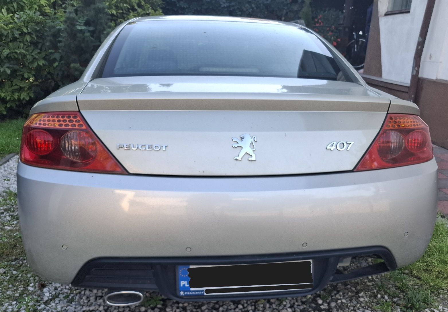 Zdjęcie przedstawia tylną część nadwozia sportowego samochodu osobowego Peugeot 407 Coupé w kolorze beżowo-popielatym.