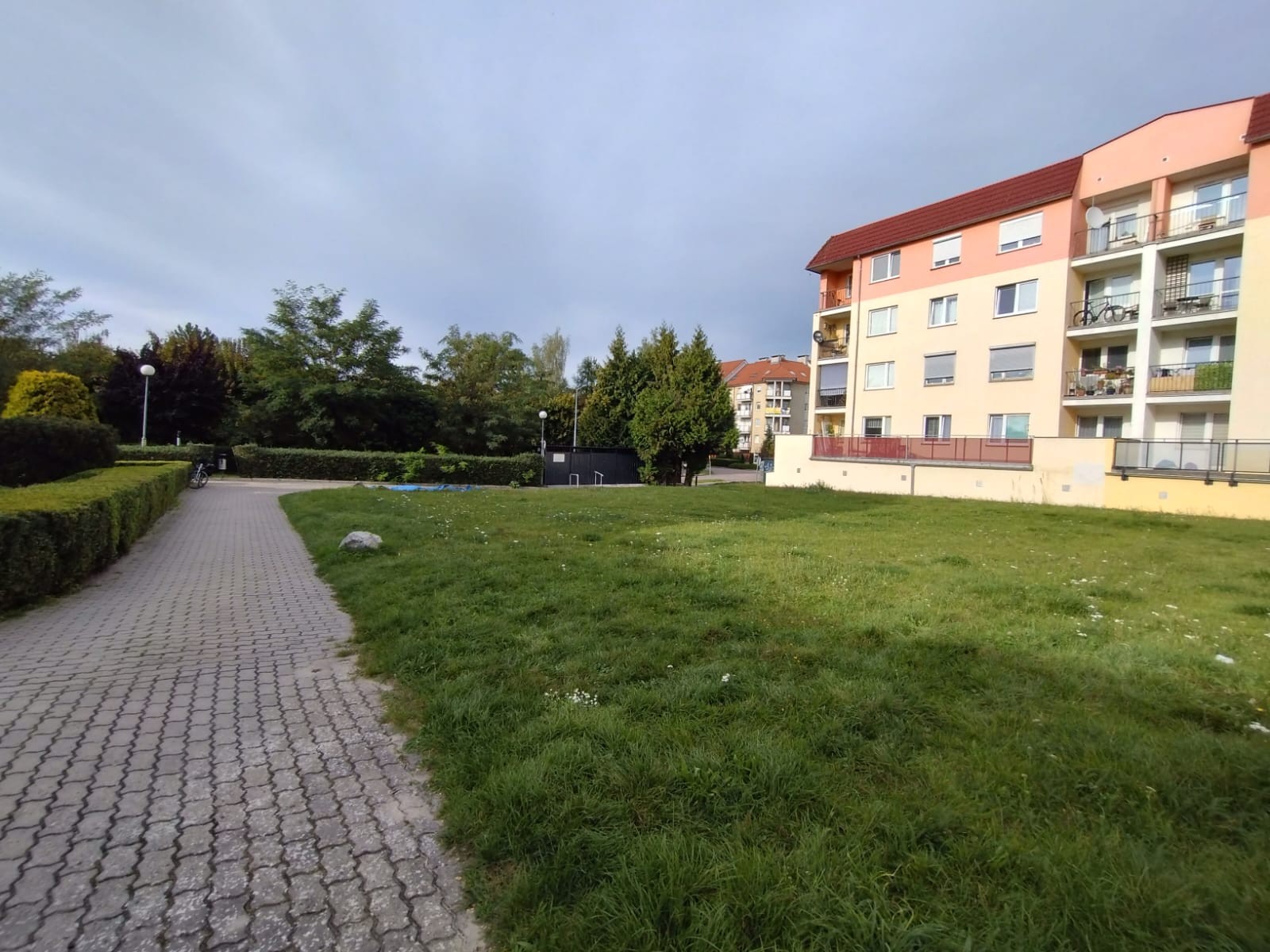 jest to teren osiedla mieszkaniowego, na głównym planie skwer z trawnikiem, po lewej stronie chodnik z kostki brukowej