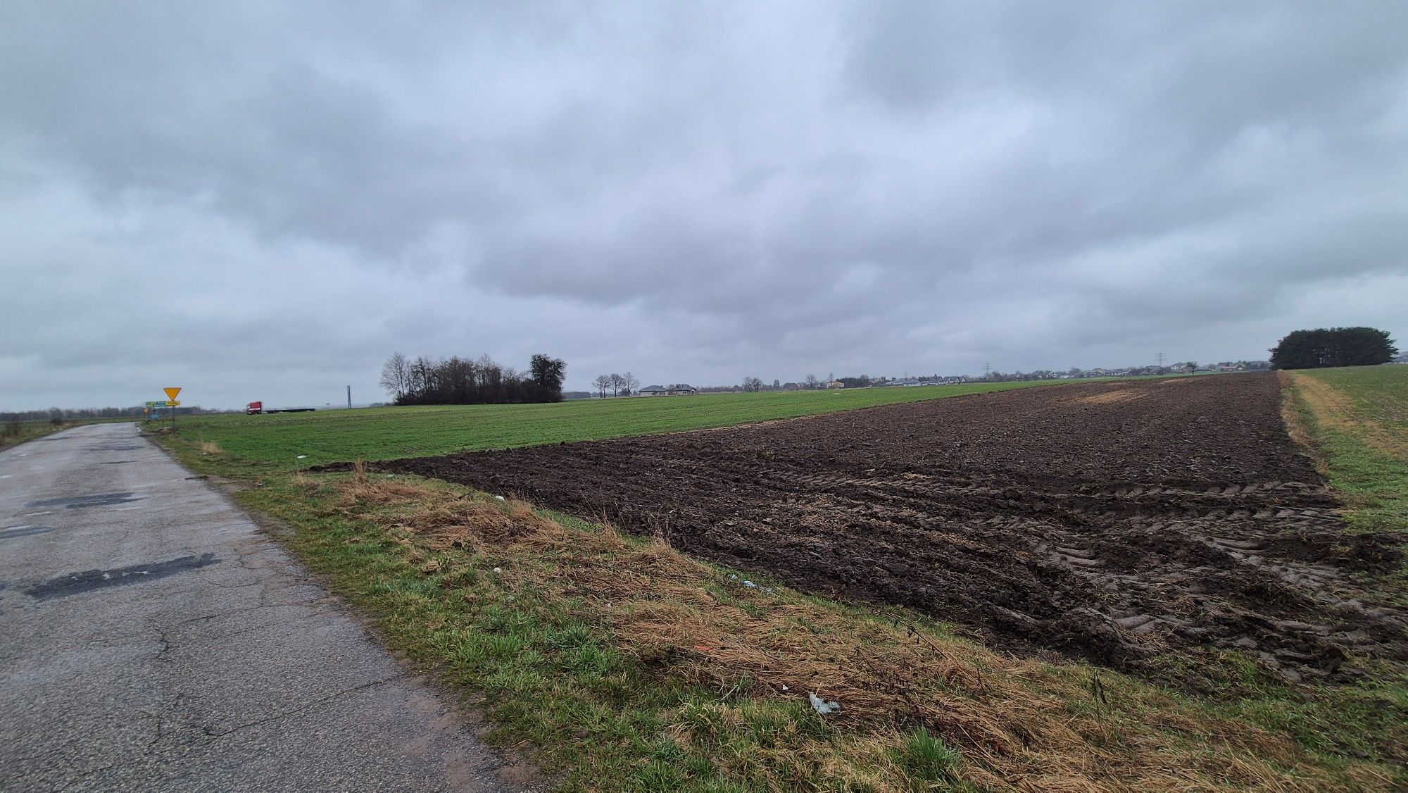 Zaorane pole i zielona łąka obok asfaltowej drogi w pochmurny dzień.