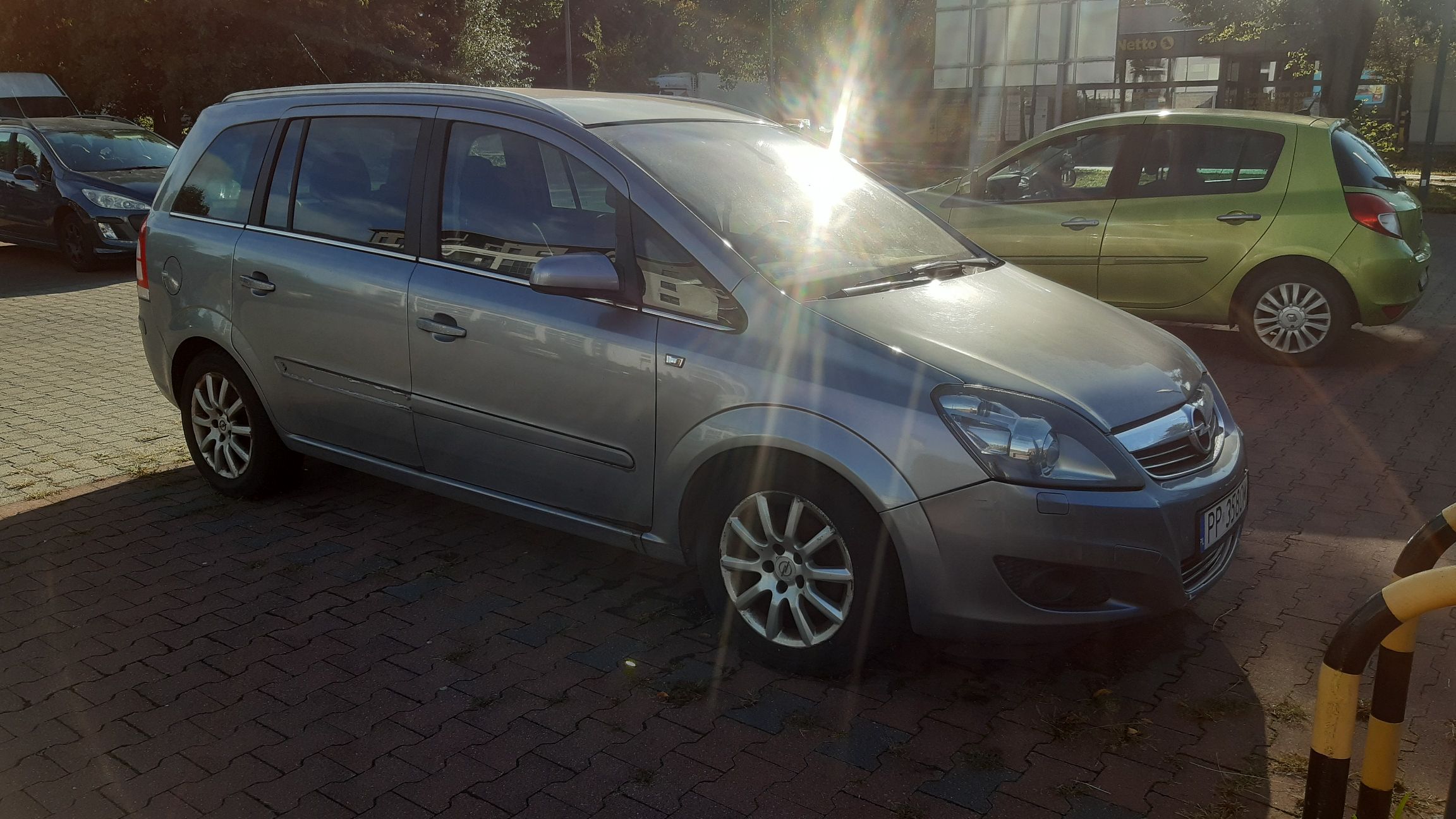 Srebrny samochód osobowy Opel Zafira, sfotografowany z przodu i z lewej strony