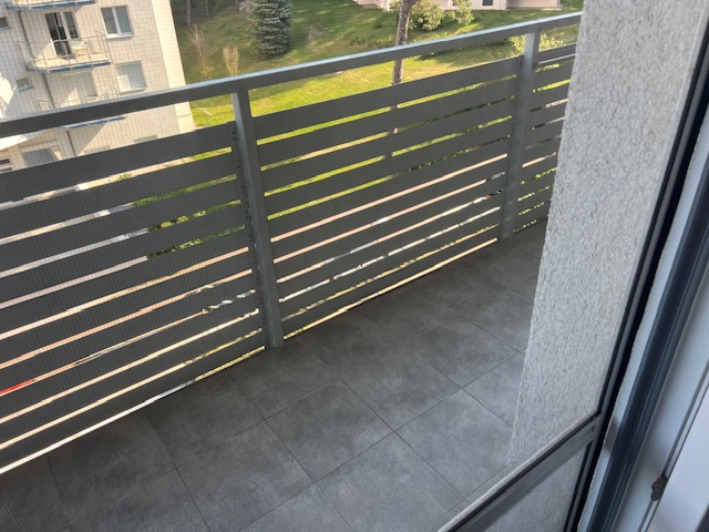 Balkon z ciemnoszarymi płytkami podłogowymi i nowoczesną metalową balustradą z poziomych lameli.