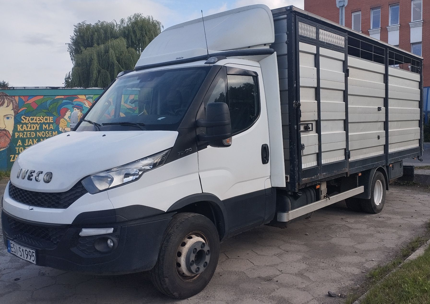 Białe Iveco Daily z lewego profilu od przodu. Zabudowa do przewozu zwierząt z aluminiowymi panelami.