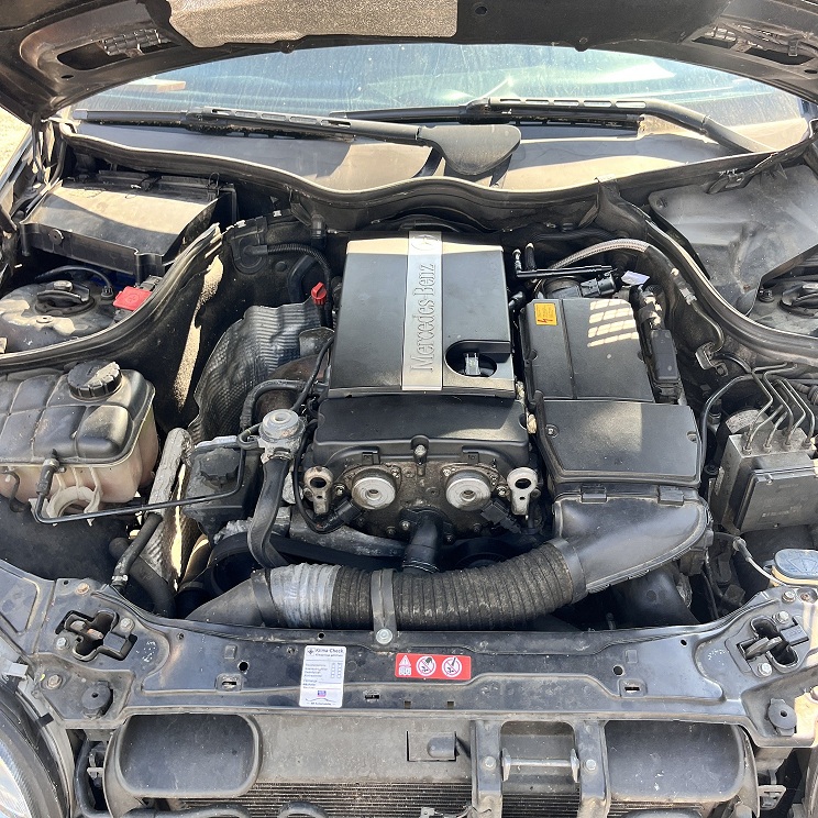 Silnik samochodu Mercedes-Benz C 180 z otwartą maską, widoczne elementy układu dolotowego, akumulator i inne podzespoły.