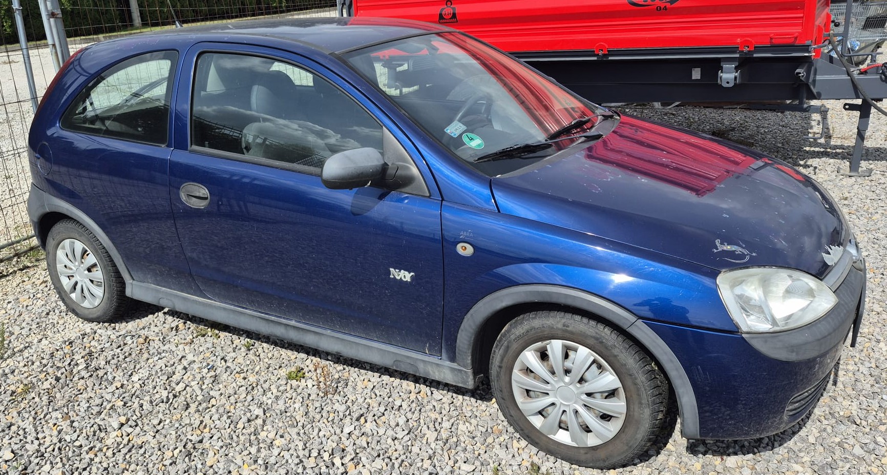 Prawa strona granatowego pojazdu OPEL CORSA C. Srebrne kołpaki na kołach, plastikowe nakładki na progach.