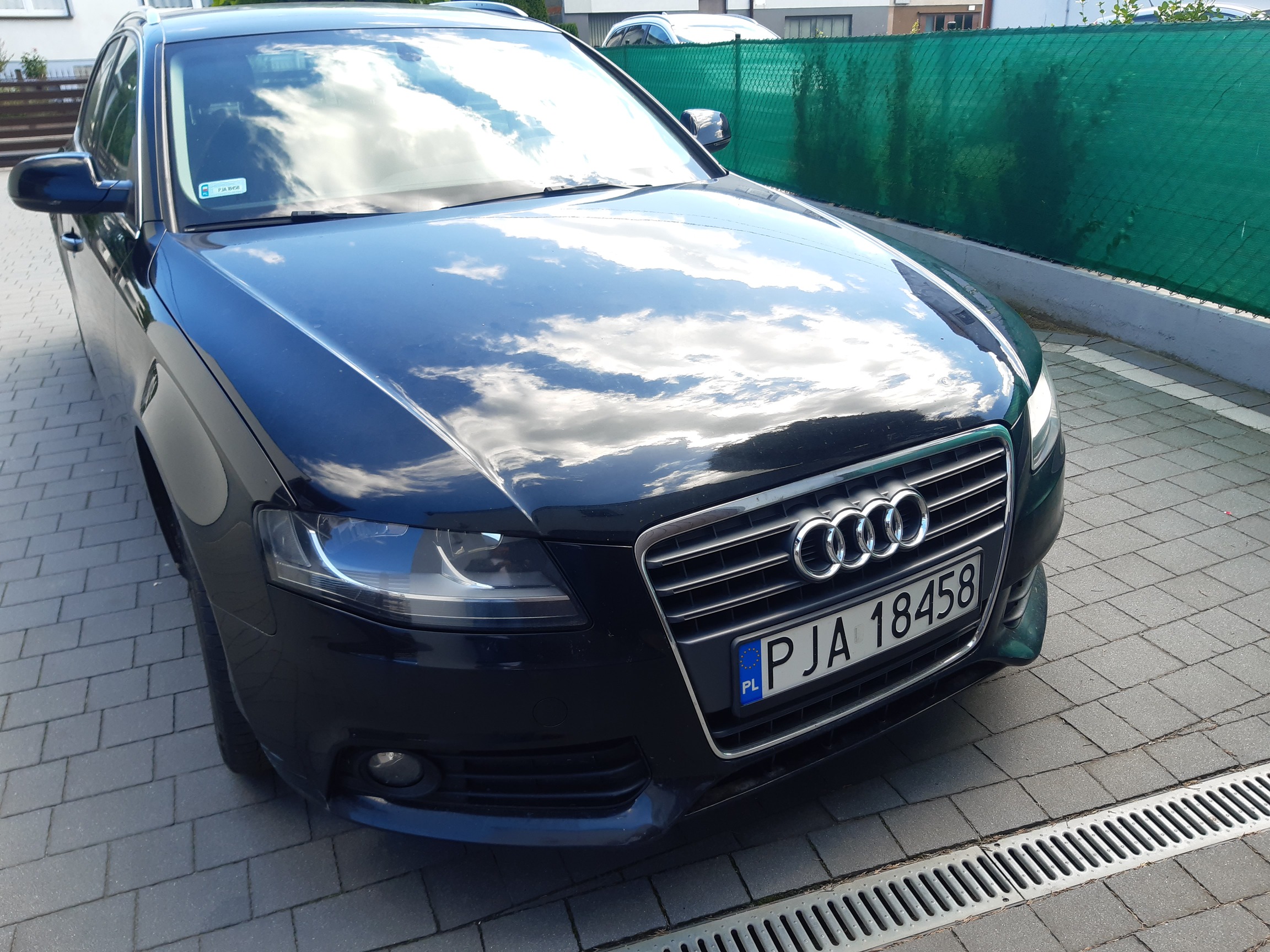 Czarny przód Audi A4 B8. Widoczna błyszcząca maska, reflektory, duży chromowany grill z logo marki i tablica rejestracyjna.