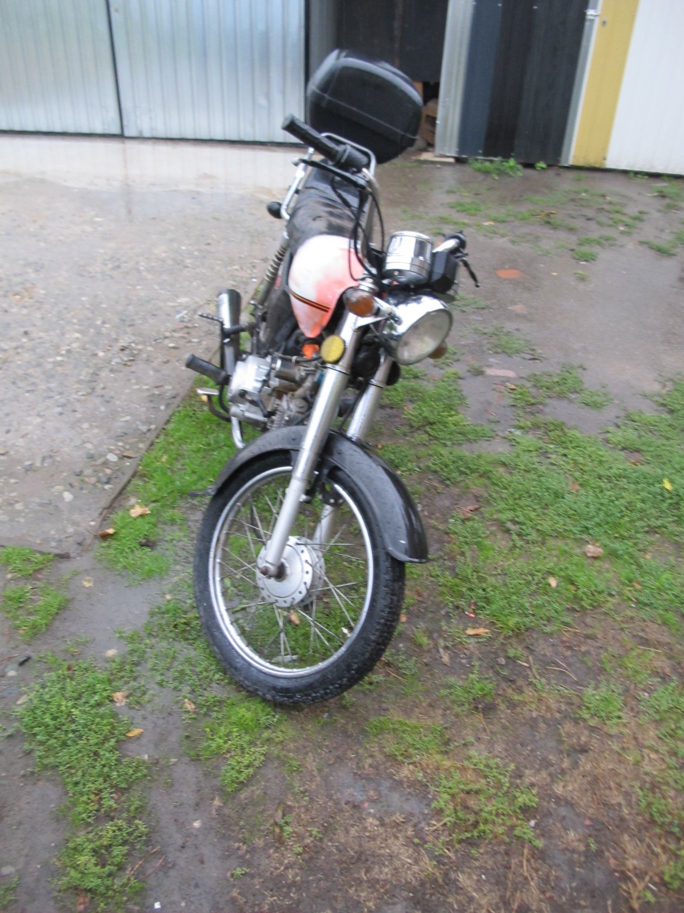 Przód motoroweru z widocznym reflektorem, kierunkowskazami, błotnikiem i przednim kołem.
