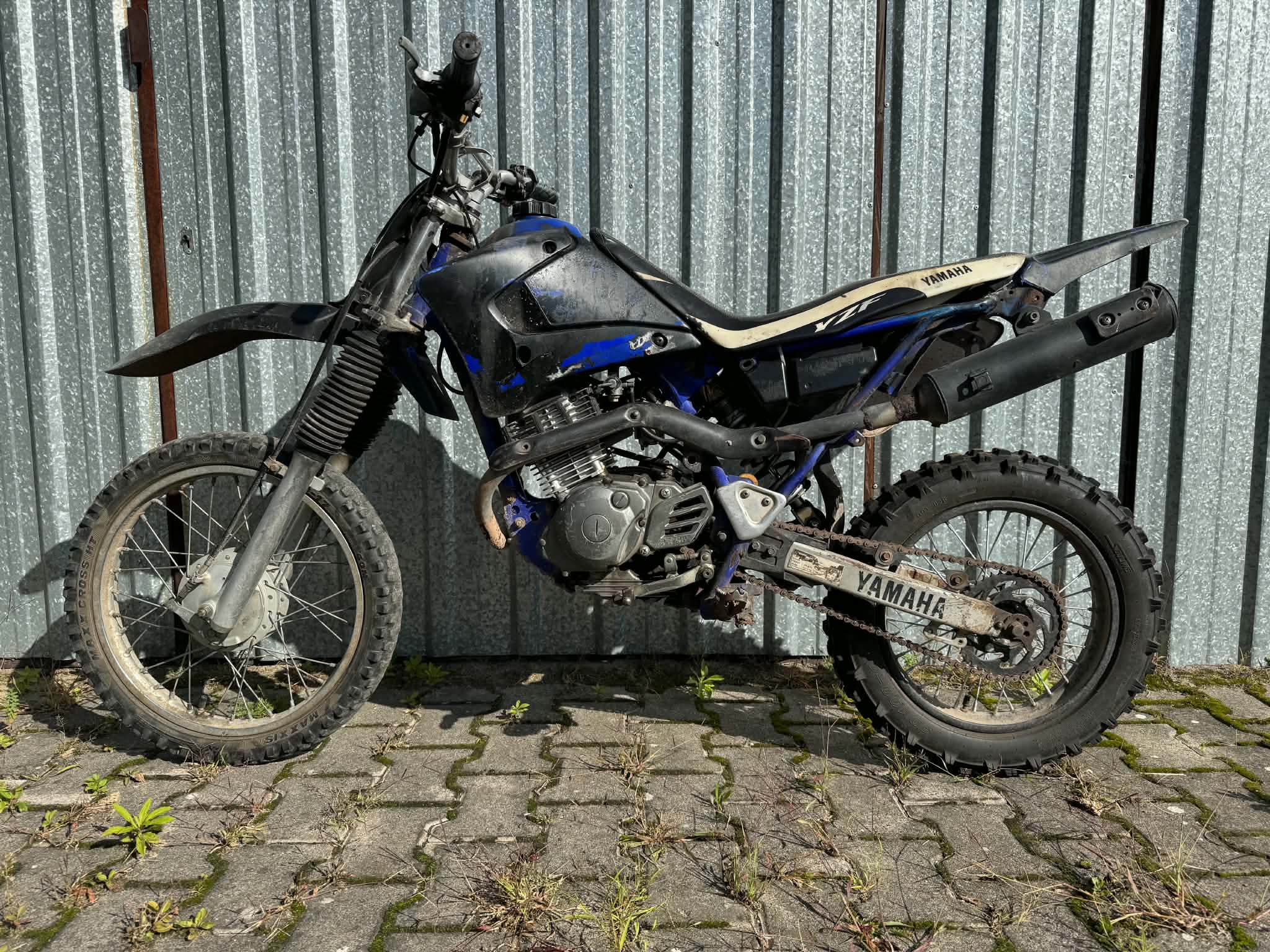 Motocykl terenowy Yamaha. Ma niebieskie i czarne elementy nadwozia, a jego siedzenie jest beżowe z widocznym logo Yamaha.