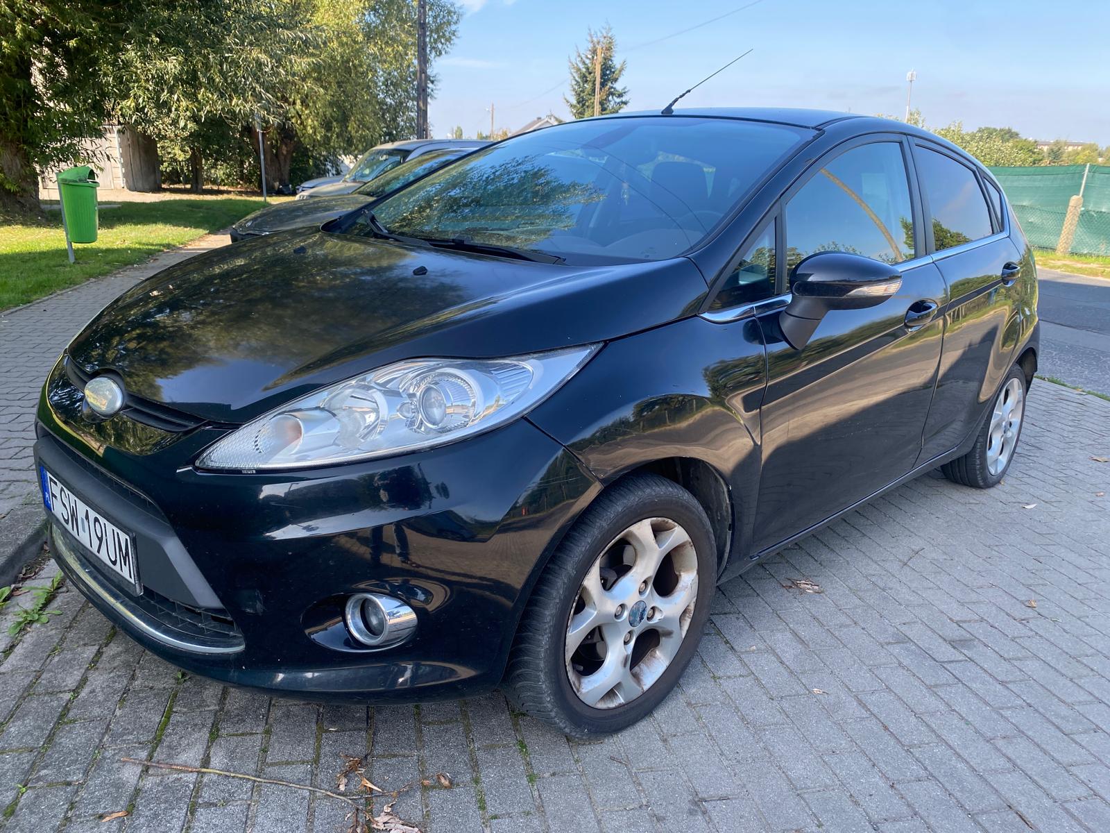 Lewa strona Forda Fiesty koloru czarnego. Felgi aluminiowe 4 ramienne aluminiowe 15 calowe.