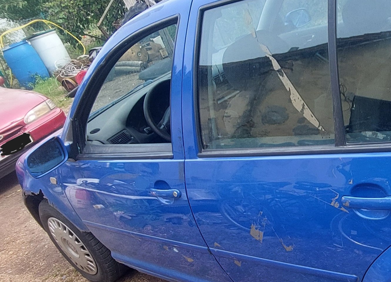 Lewy bok niebieskiego Volkswagena Golfa, widoczne ubytki w skorodowanym przednim błotniku, wybita szyba w drzwiach kierowcy.