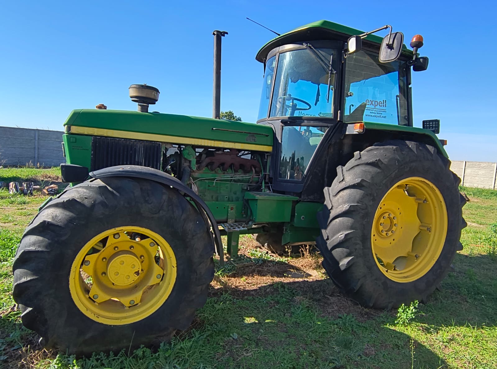 traktor posiadający duże bieżnikowane opony, przeszkloną kabinę kierowcy oraz charakterystyczną konstrukcję silnika.