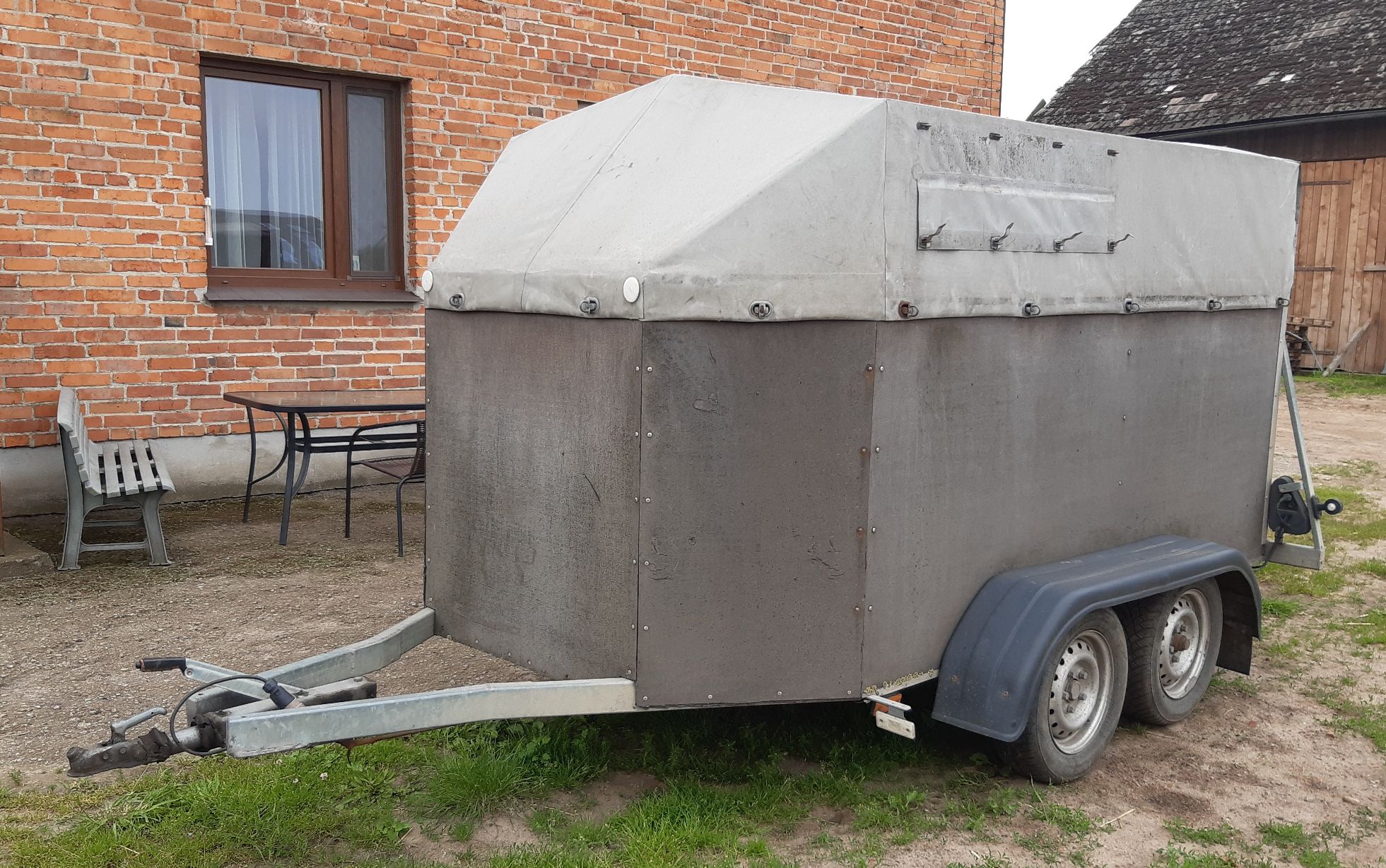 Szara, zakryta przyczepa do transportu żywych zwierząt, posiadająca metalowy stelaż, widziana od przodu.