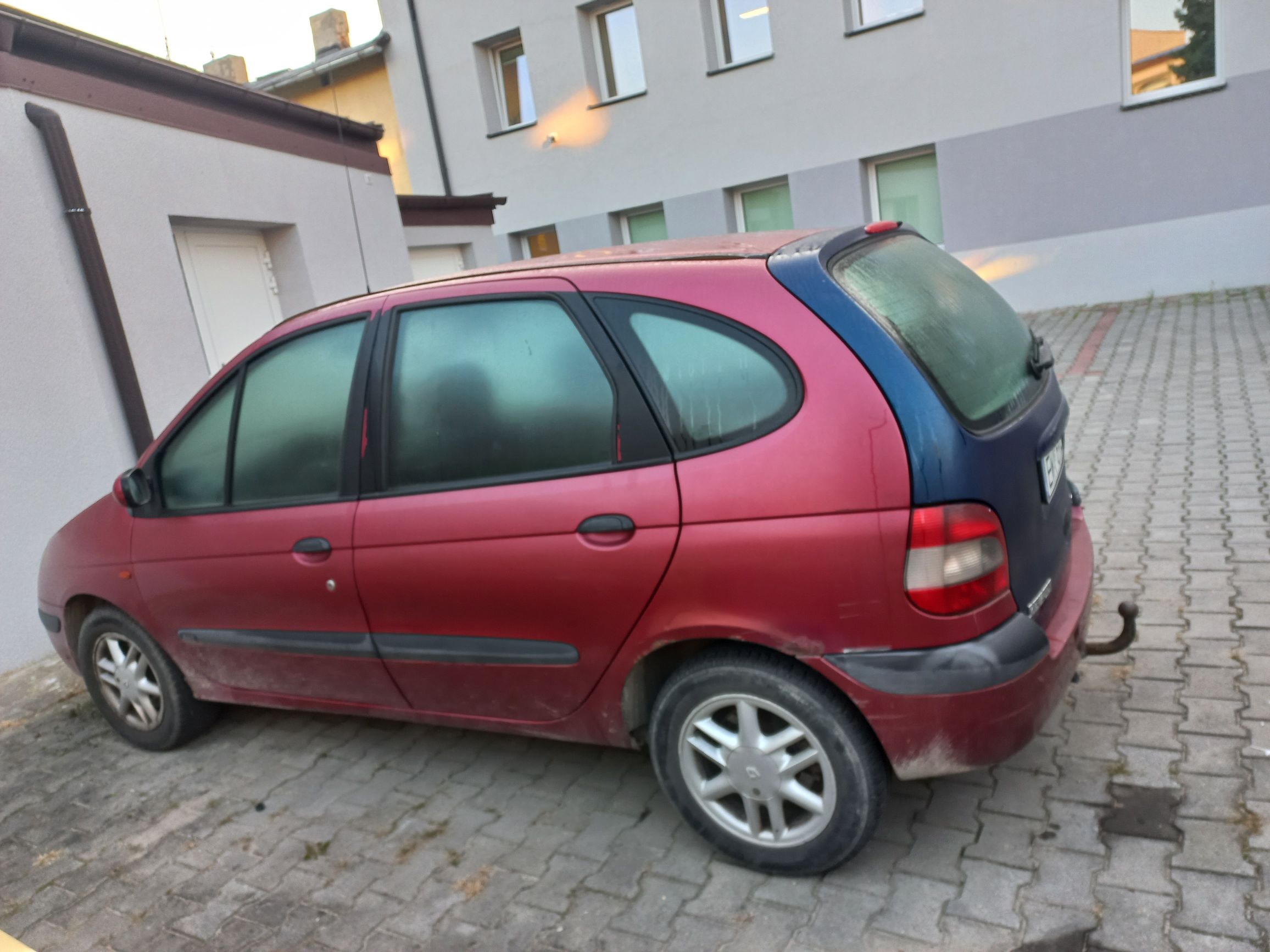 Czerwono-niebieskie Renault Scenic pierwszej generacji z mocno zaparowanymi szybami, zaparkowane na brukowanym podwórku.