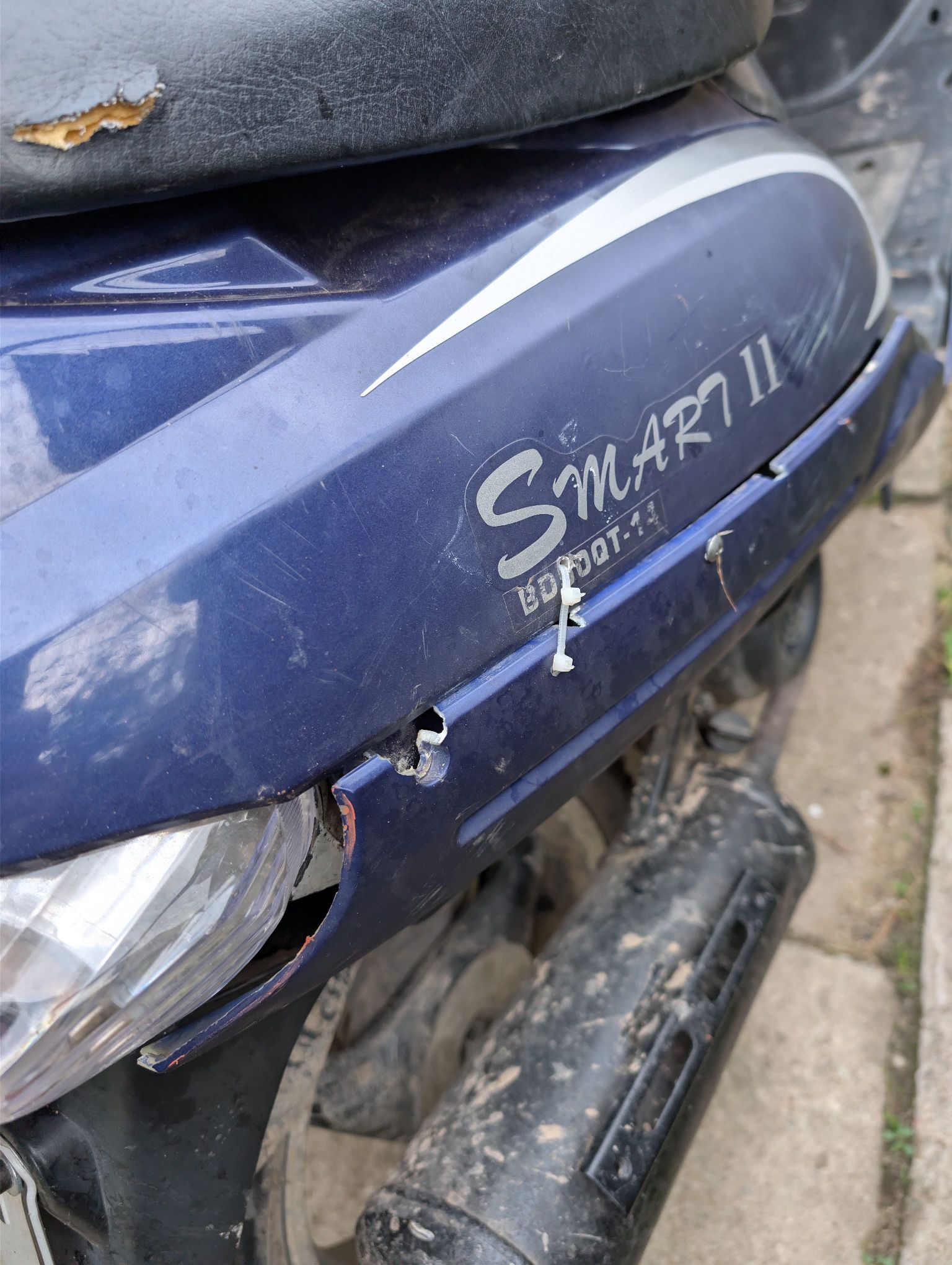 Na zdjęciu widać obudowę przednią porysowaną, miejscami popękana. Mocowanie osłony przymocowane opaską zaciskową.