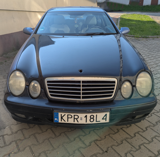 Przód samochodu Mercedes-Benz CLK 200. Maska oraz zderzak w kolorze ciemnozielonym, brak znaku mercedesa na masce.