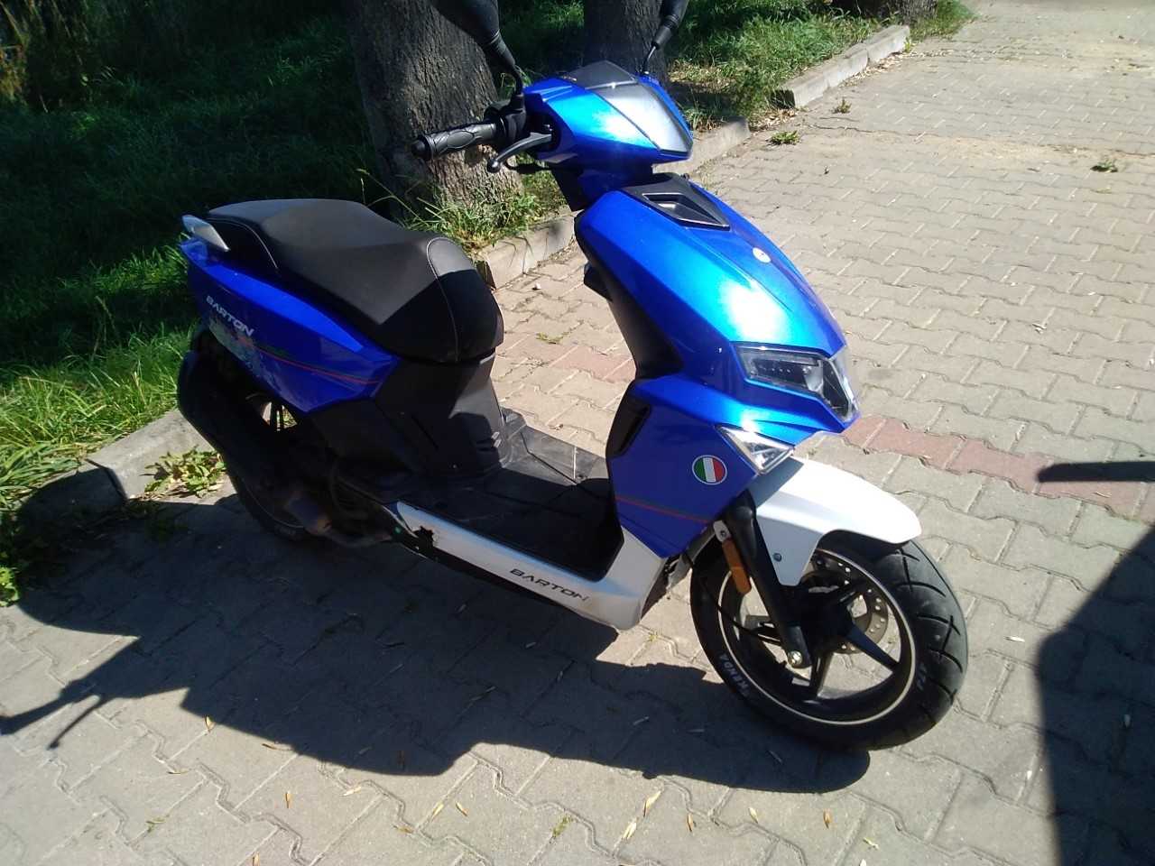 Motorower koloru niebiesko-białego. Pojazd ma czarne siedzenie, reflektory LED.
