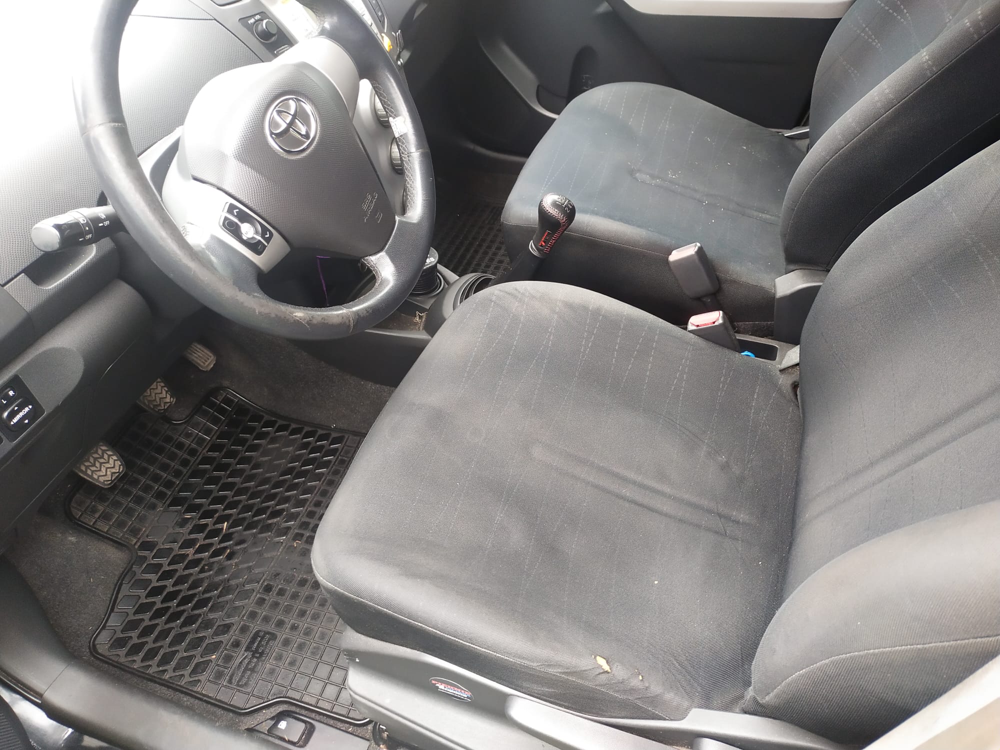 Po lewej stronie u góry widoczna jest czarna, trójramienna kierownica z metalicznymi elementami i logo Toyoty na środku.