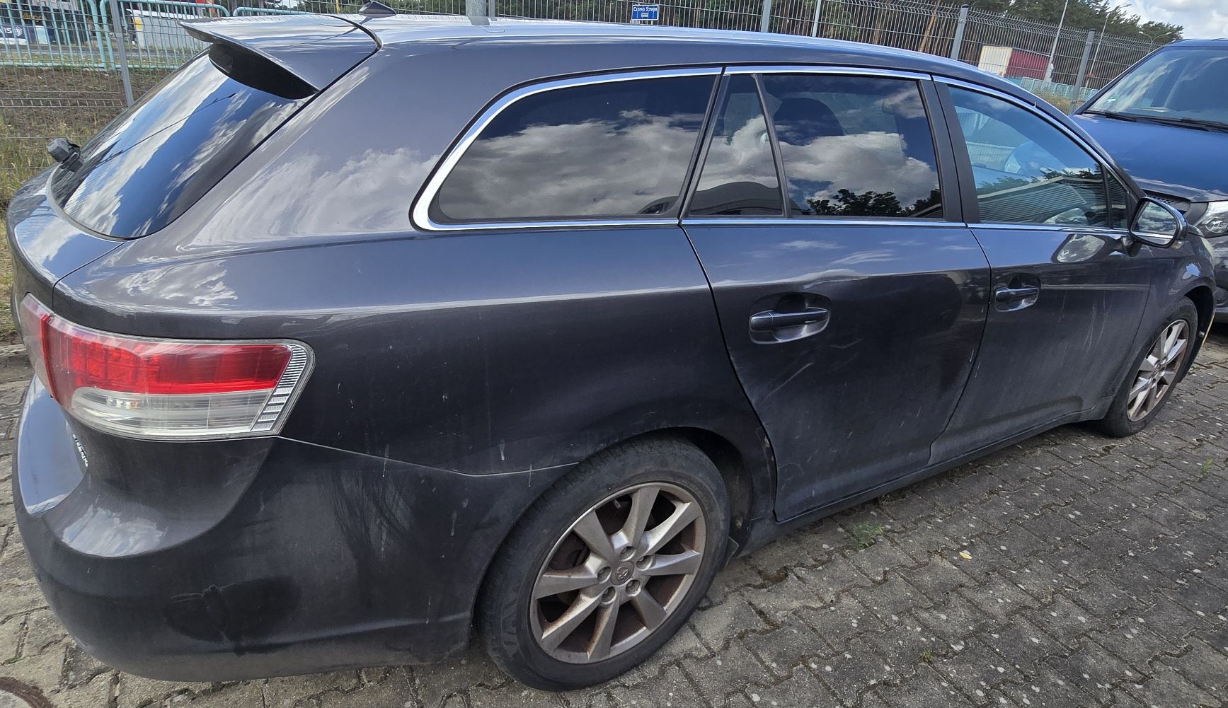 Prawy bok grafitowej Toyoty Avensis z widocznymi niewielkimi zarysowaniami lakieru