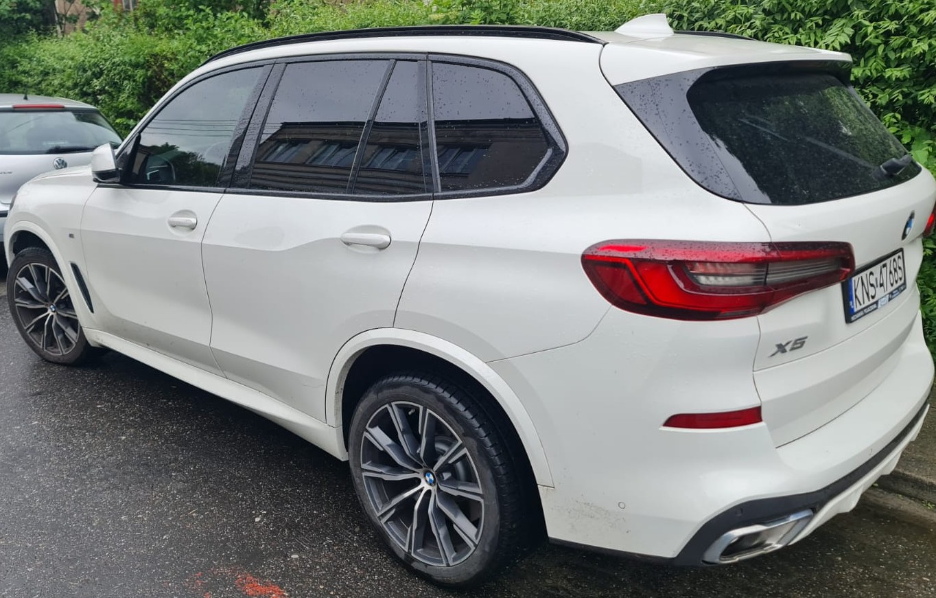 Białe BMW X5 z widocznymi tylnymi reflektorami i tablicą rejestracyjną.