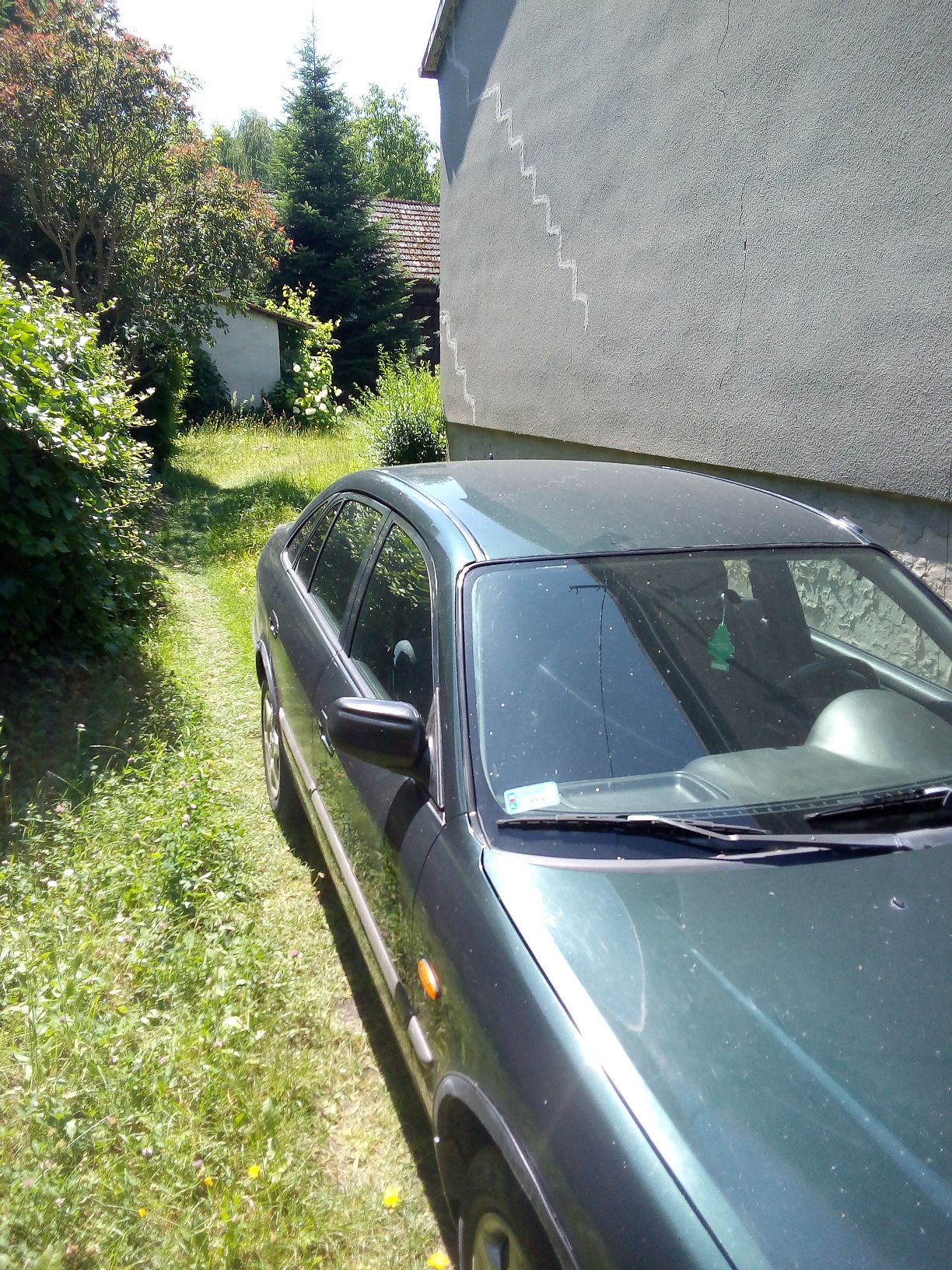 Ciemnozielony samochód osobowy marki Mazda 626 widziany z przodu i boku