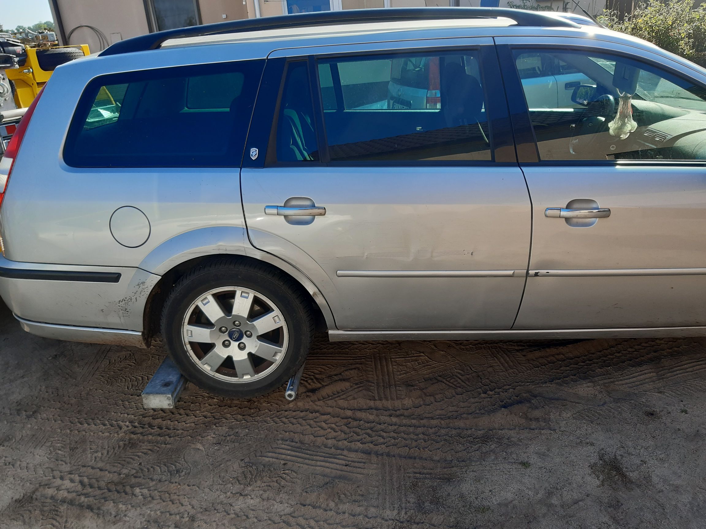 Srebrny Ford Mondeo kombi z profilu. Ma przyciemniane tylne szyby, i czarne relingi dachowe
