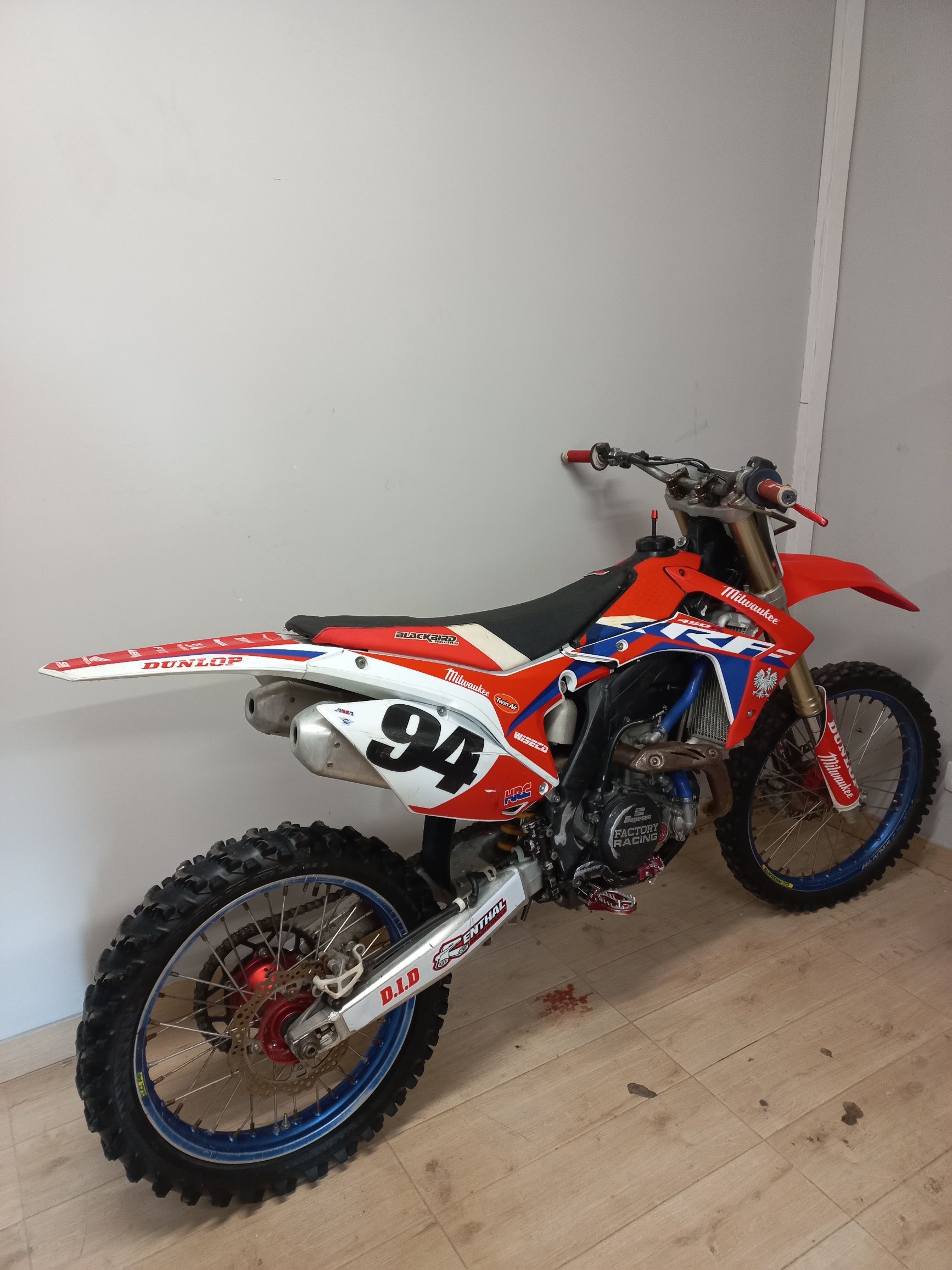 Motocykl crossowy Honda CRF z numerem 94, widok z profilu od strony wydechu w jasnym pokoju