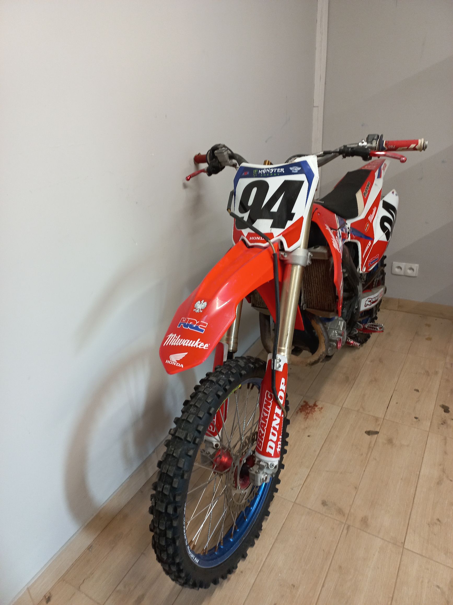 Czerwony motocykl crossowy Honda z numerem startowym 94, sfotografowany od przodu w jasnym pomieszczeniu