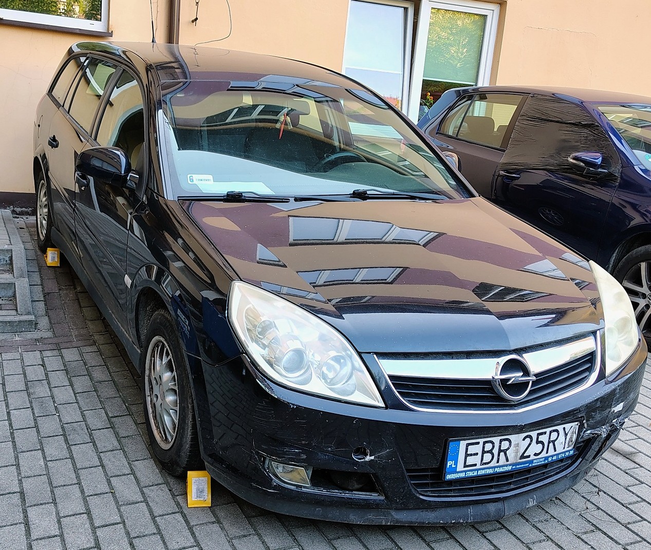 Granatowy samochód osobowy typu kombi. Widoczne zarysowania i wgniecenia na przednim zderzaku.