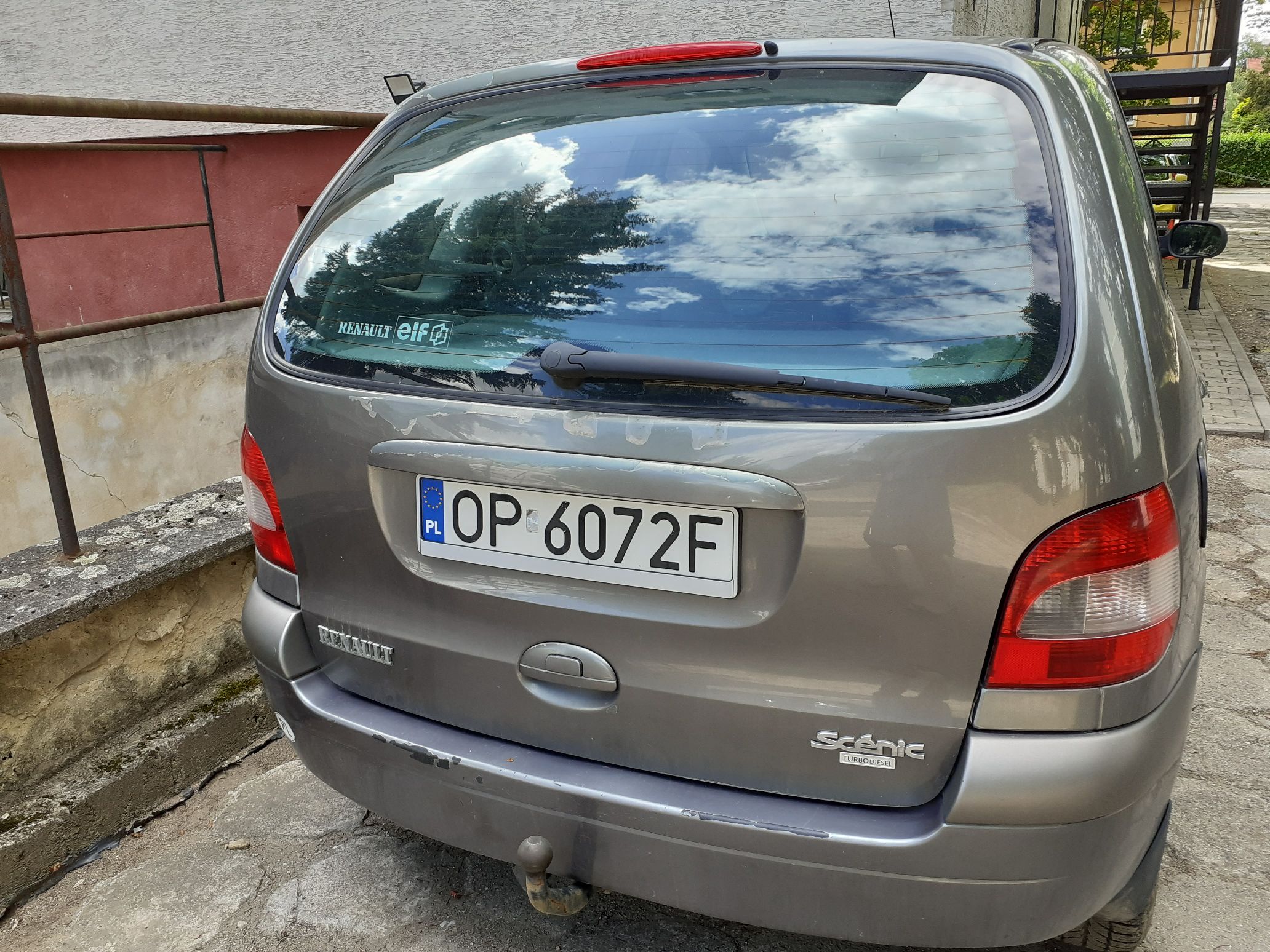 Srebrny minivan Renault Scenic, widoczny od tyłu, z polską tablicą rejestracyjną OP 6072F i hak holowniczy.
