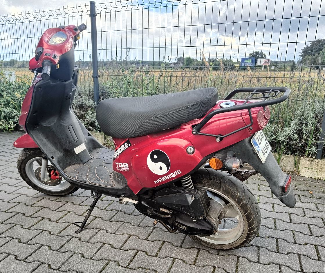 Tył oraz lewy bok motoroweru w kolorze czerwonym, widoczne zadrapania na obudowach pojazdu.