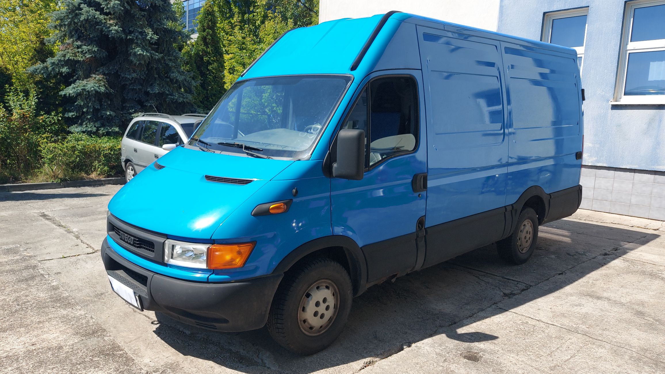 Niebieski samochód dostawczy Iveco Daily - furgon (blaszak). Pojazd ma wysoki dach, czarne zderzaki i szerokie listwy ochronne.