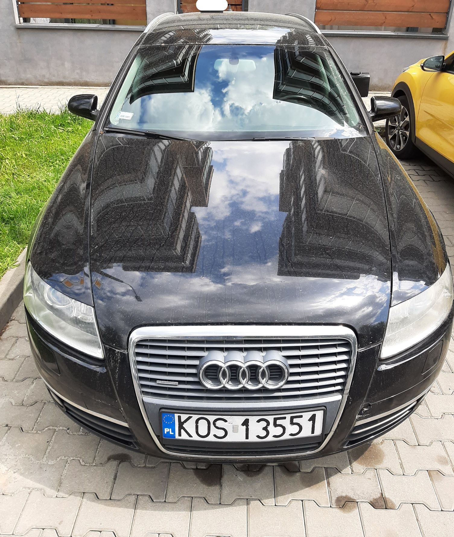 Czarny samochód Audi z zamkniętą maską, z przodu widoczny chromowany grill z logo i rejestracją