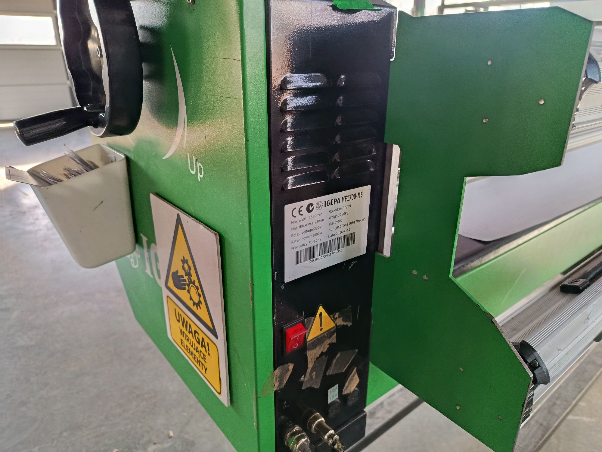 Wielkoformatowy laminator rolowy w kolorze zielono-czarnym, stojący na kołkach w warsztacie lub drukarni. Tabliczka znamionowa.