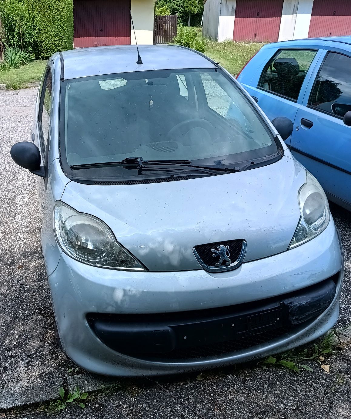 Zdjęcie przedmiotu. Przód samochodu w kolorze srebrnym. Widoczna maska i szyba przednia samochodu