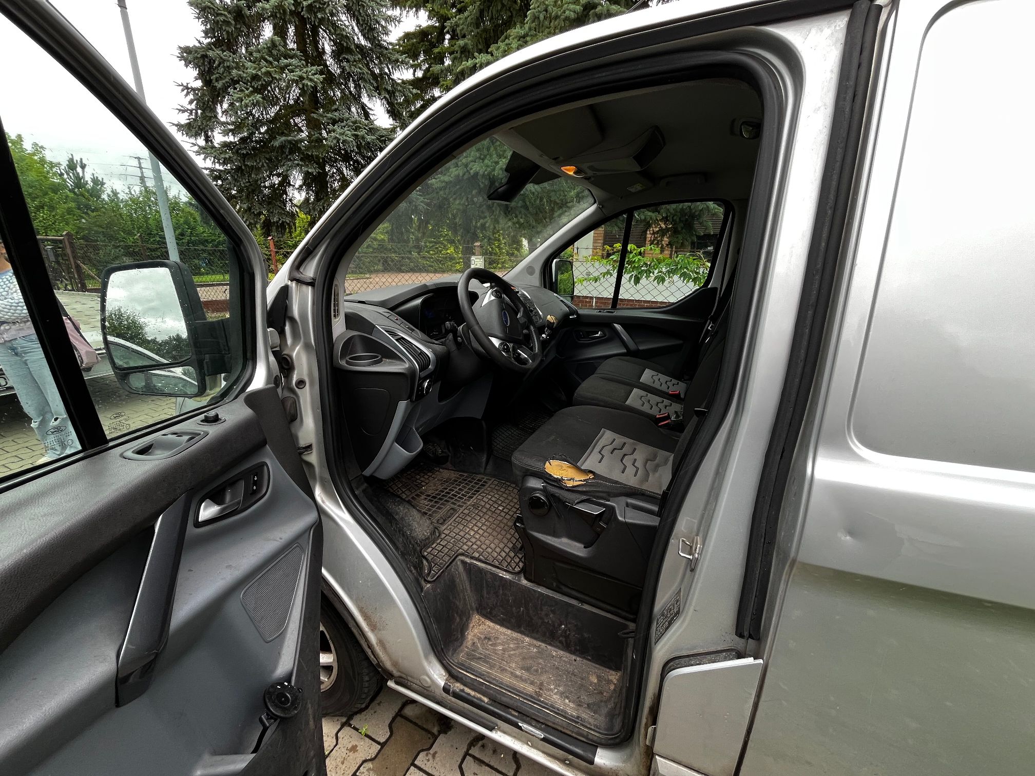 srebrny Ford Transit Custom z otwartymi drzwiami od strony kierowcy widoczne przetarcie tapicerki w fotelu kierowcy